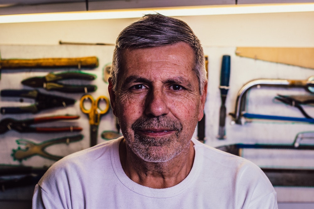 John with clothing on in front of a wall with tools smiling