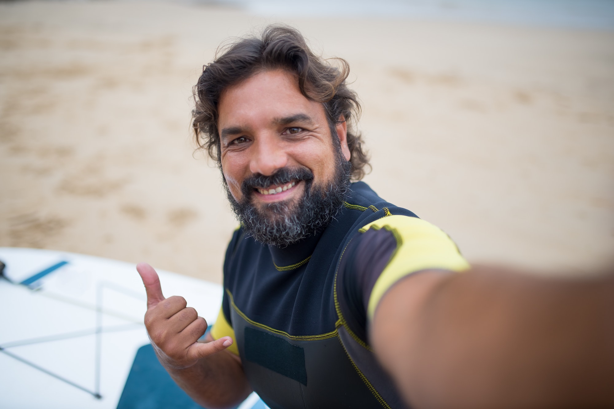 Andy at a beach with a surf board with clothing on smiling